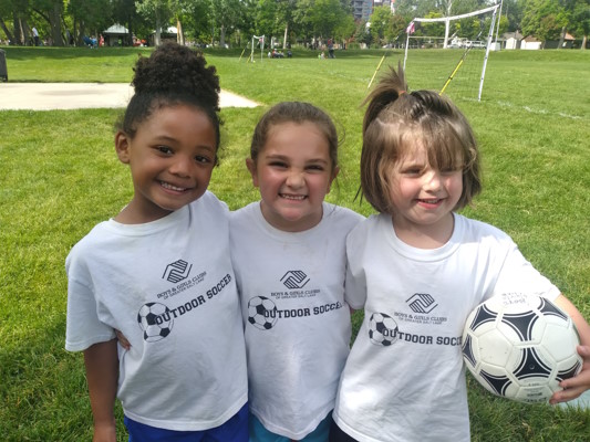 Three girls in white team shirts with a soccer ball
